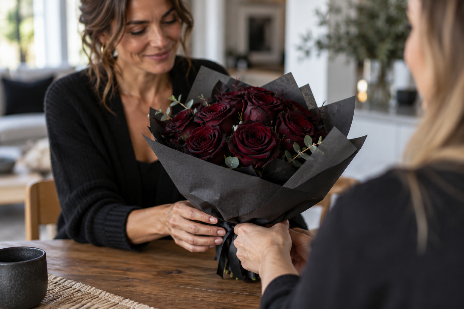 A woman receives a wrapped bouquet of dark burgundy roses from a friend.